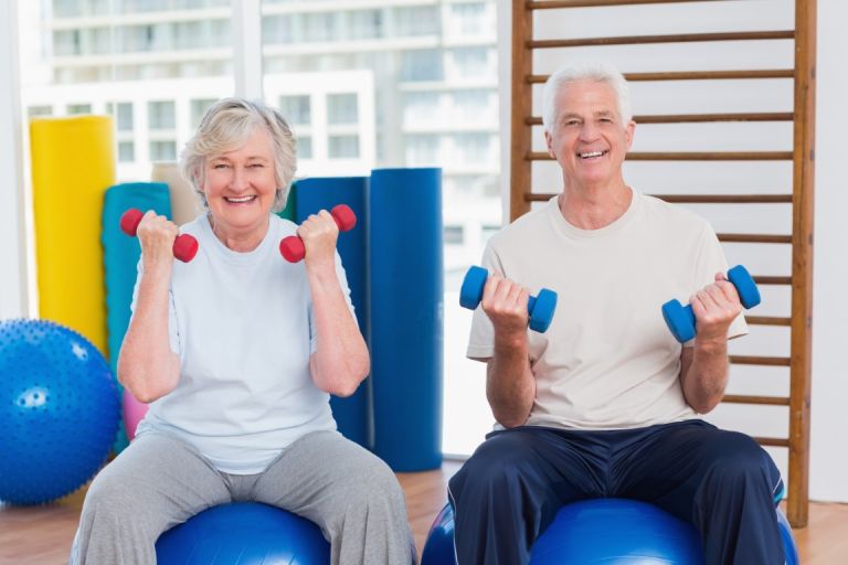 happy senior couple lifting dumbbells on exercise ball